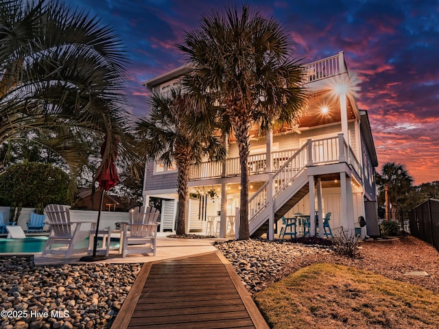 back house at dusk with a patio, a balcony, and a fenced in pool