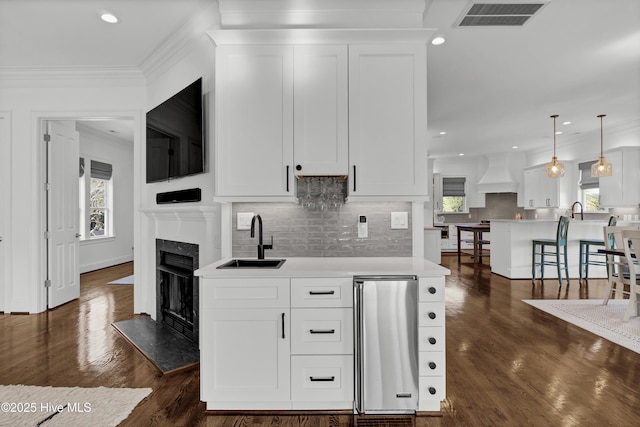 kitchen with white cabinetry, sink, pendant lighting, and custom range hood