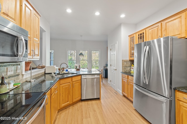 kitchen featuring dark stone countertops, pendant lighting, sink, light wood-type flooring, and appliances with stainless steel finishes