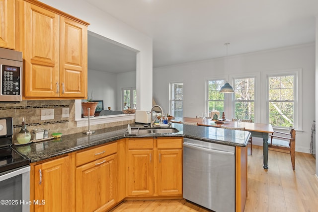 kitchen with kitchen peninsula, sink, hanging light fixtures, stainless steel appliances, and dark stone counters