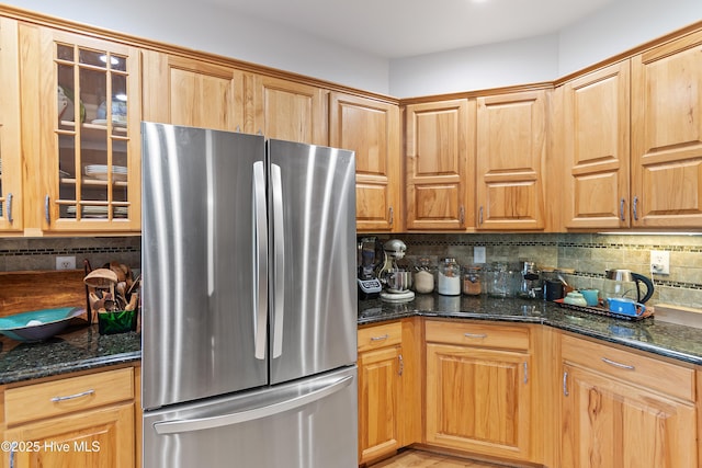 kitchen featuring decorative backsplash, stainless steel fridge, and dark stone countertops