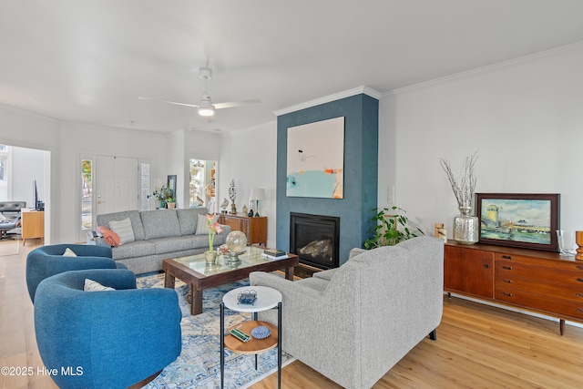 living room with ceiling fan, crown molding, a fireplace, and light hardwood / wood-style flooring