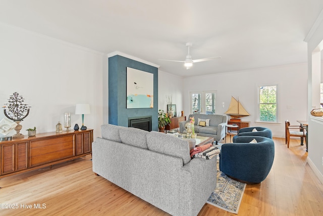 living room featuring ceiling fan, wood-type flooring, a fireplace, and ornamental molding