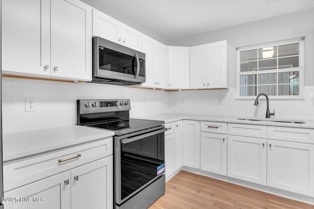 kitchen with appliances with stainless steel finishes, light hardwood / wood-style flooring, white cabinetry, and sink