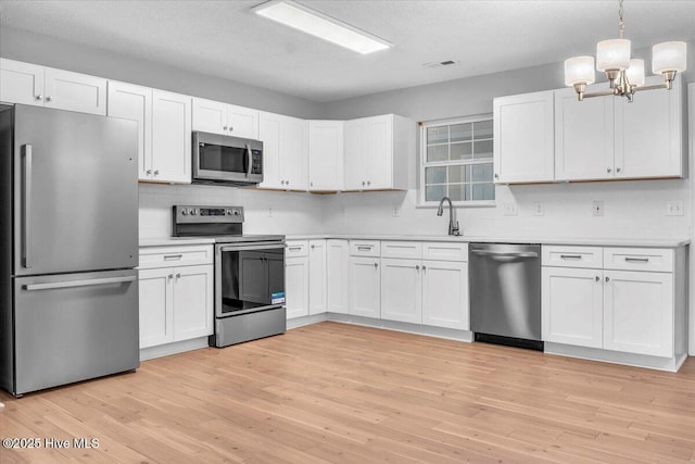 kitchen with appliances with stainless steel finishes, light wood-type flooring, a textured ceiling, white cabinets, and hanging light fixtures