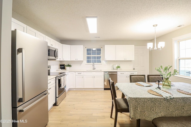 kitchen with appliances with stainless steel finishes, sink, pendant lighting, a notable chandelier, and white cabinetry