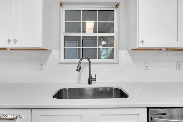 kitchen with stainless steel dishwasher, white cabinetry, sink, and tasteful backsplash