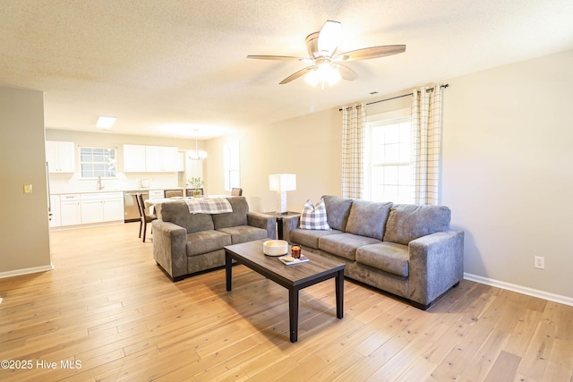 living room with a textured ceiling, light hardwood / wood-style flooring, ceiling fan with notable chandelier, and sink