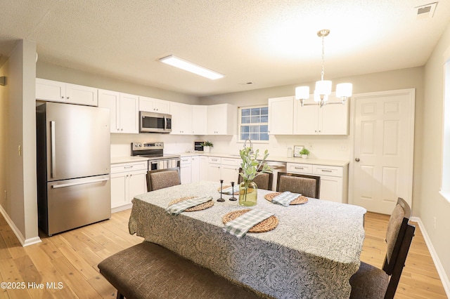 kitchen with white cabinetry, hanging light fixtures, stainless steel appliances, an inviting chandelier, and light hardwood / wood-style flooring