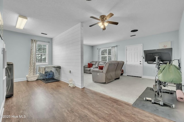 living room featuring hardwood / wood-style floors, ceiling fan, wood walls, and a textured ceiling