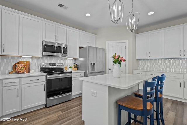 kitchen featuring stainless steel appliances, a kitchen island, a notable chandelier, pendant lighting, and white cabinets