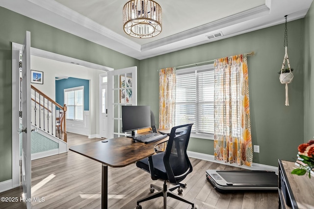 home office with light hardwood / wood-style flooring, a raised ceiling, and ornamental molding