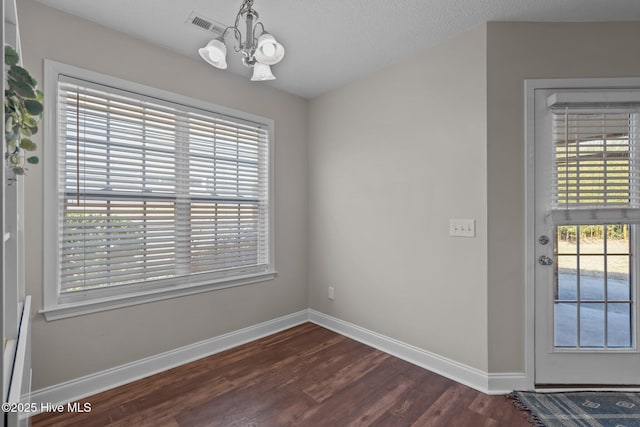 interior space with a textured ceiling, dark wood-type flooring, plenty of natural light, and a notable chandelier