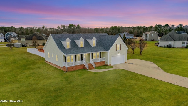 new england style home with covered porch, a yard, and a garage