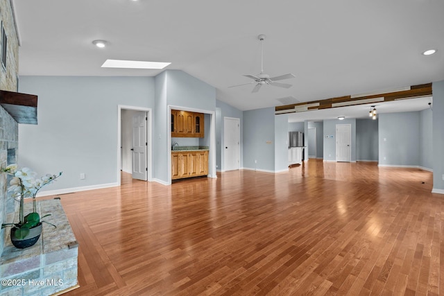 unfurnished living room featuring ceiling fan, a fireplace, lofted ceiling with skylight, and light wood-type flooring