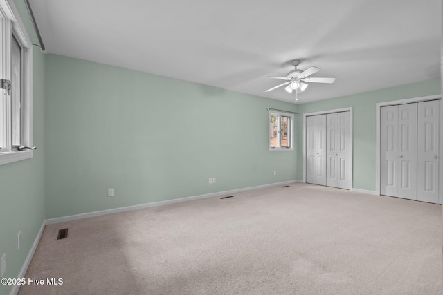 unfurnished bedroom featuring ceiling fan, light carpet, and two closets