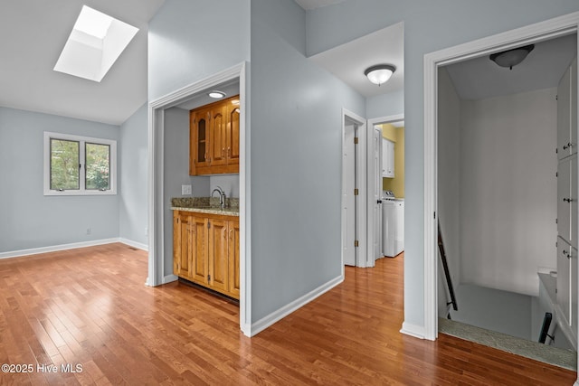 interior space featuring light stone countertops, sink, washer / clothes dryer, lofted ceiling with skylight, and light hardwood / wood-style floors