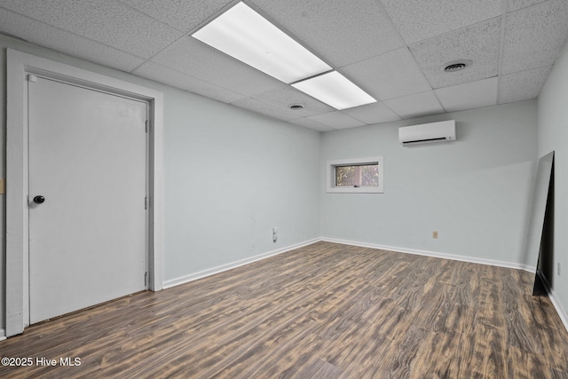 basement with an AC wall unit, a paneled ceiling, and dark wood-type flooring