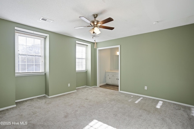 unfurnished bedroom with ceiling fan, ensuite bath, light carpet, and a textured ceiling