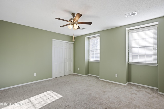 unfurnished bedroom featuring ceiling fan, a textured ceiling, a closet, and light carpet