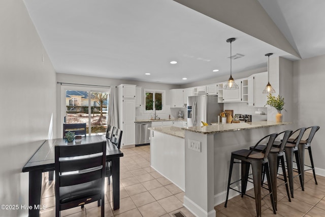 kitchen featuring kitchen peninsula, decorative backsplash, light tile patterned floors, appliances with stainless steel finishes, and white cabinetry