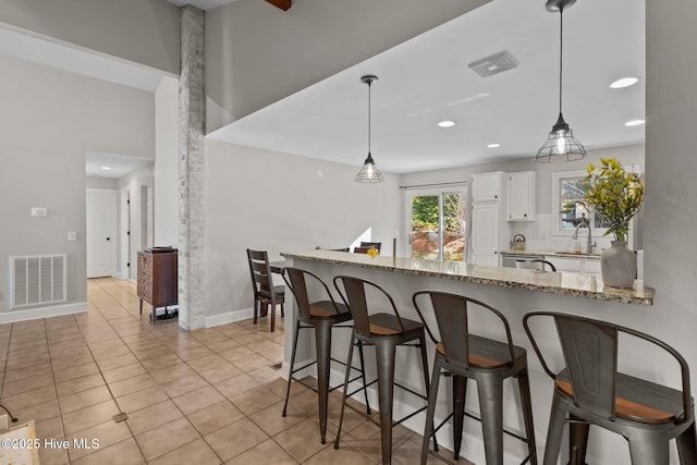 kitchen with pendant lighting, sink, kitchen peninsula, light stone countertops, and white cabinetry