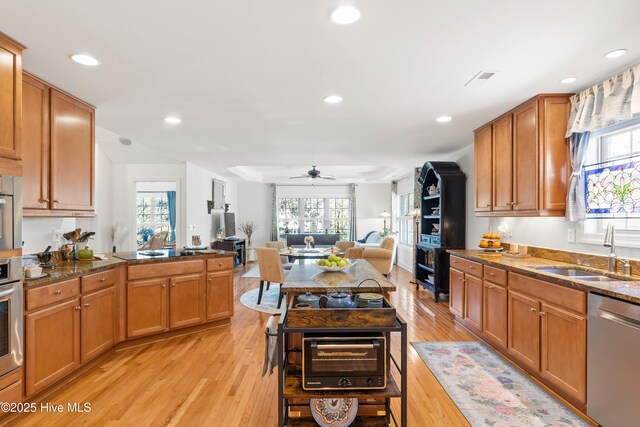 kitchen with sink, ceiling fan, appliances with stainless steel finishes, dark stone countertops, and light hardwood / wood-style floors