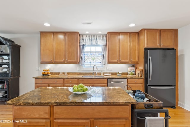 kitchen with dark stone counters, dishwasher, a center island, freestanding refrigerator, and a sink