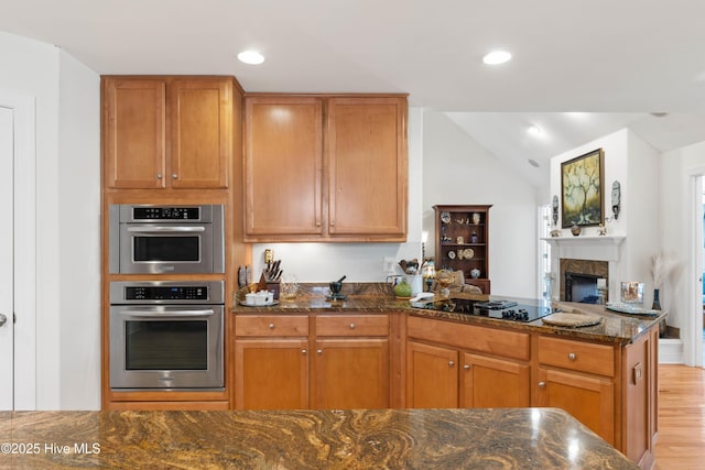 kitchen featuring dark stone countertops, stainless steel double oven, black electric cooktop, and light hardwood / wood-style floors