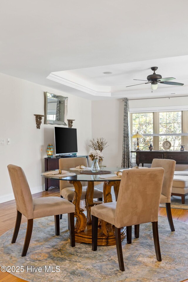 dining area featuring hardwood / wood-style flooring, ceiling fan, and a raised ceiling