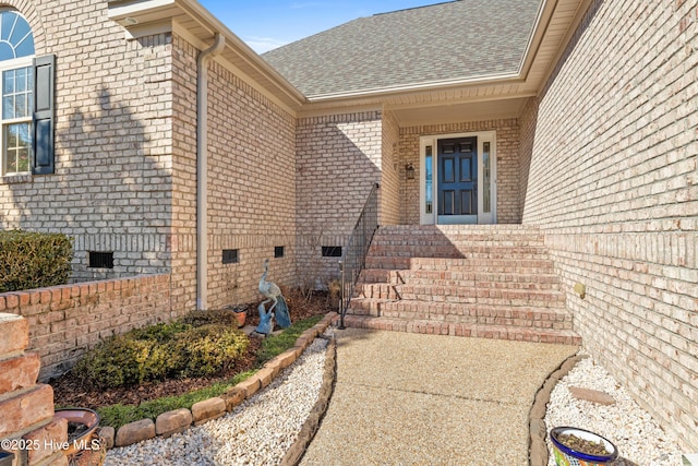 doorway to property featuring a shingled roof, crawl space, and brick siding