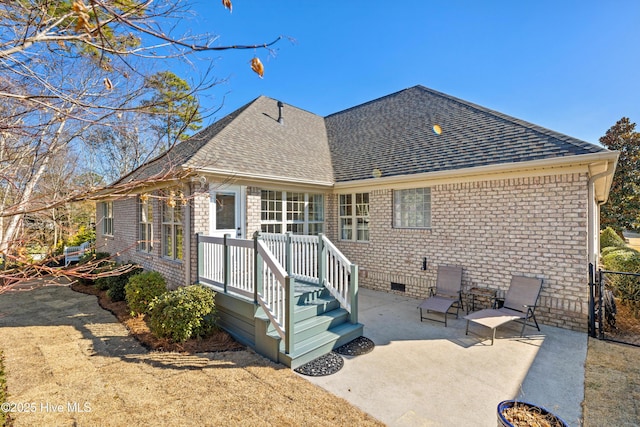 back of house featuring crawl space, roof with shingles, a patio, and brick siding