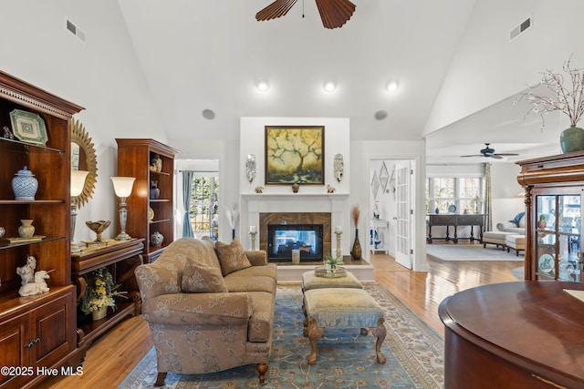 living room featuring a tile fireplace, high vaulted ceiling, light wood-type flooring, and ceiling fan