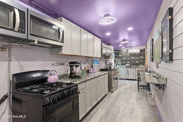 kitchen featuring white cabinetry, stainless steel appliances, light stone counters, an AC wall unit, and light hardwood / wood-style floors