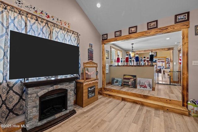 living room with light hardwood / wood-style floors, a stone fireplace, and lofted ceiling