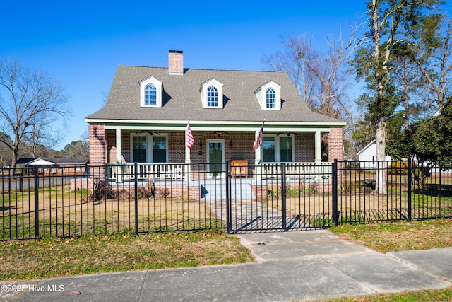 cape cod-style house featuring a fenced front yard, covered porch, brick siding, and roof with shingles