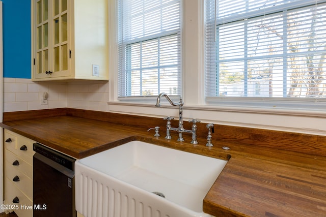 kitchen featuring tasteful backsplash, glass insert cabinets, a sink, wood counters, and dishwasher