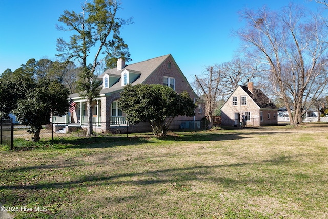 view of side of property featuring brick siding, a fenced front yard, a chimney, and a lawn