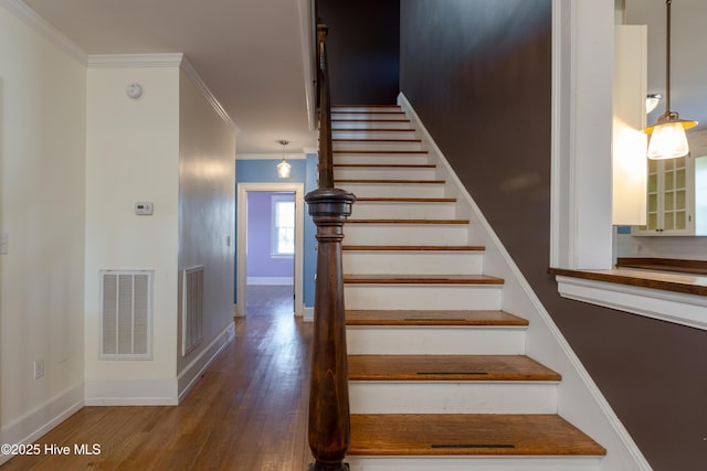 staircase featuring ornamental molding, visible vents, baseboards, and wood finished floors