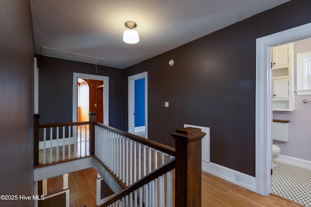 corridor with attic access, baseboards, wood finished floors, and an upstairs landing