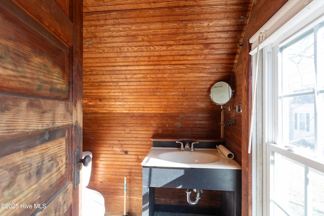 half bathroom with wooden walls, toilet, and vanity