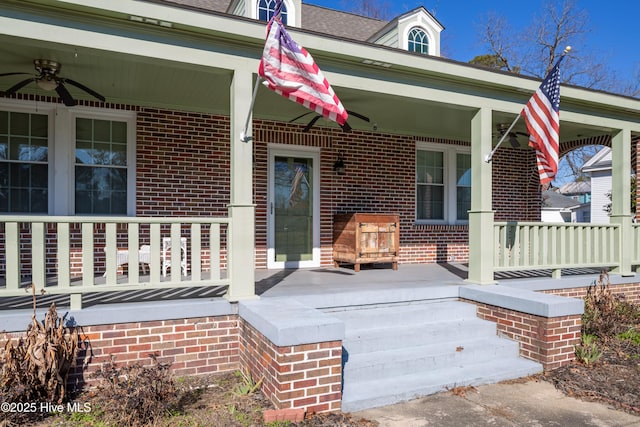 view of exterior entry featuring ceiling fan, a porch, and brick siding