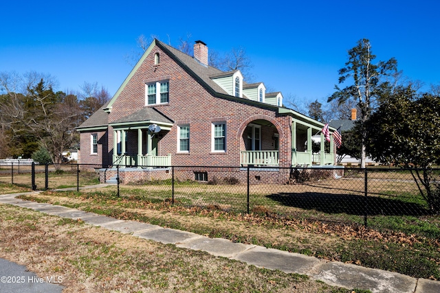 view of side of home featuring a fenced front yard, covered porch, brick siding, and a lawn