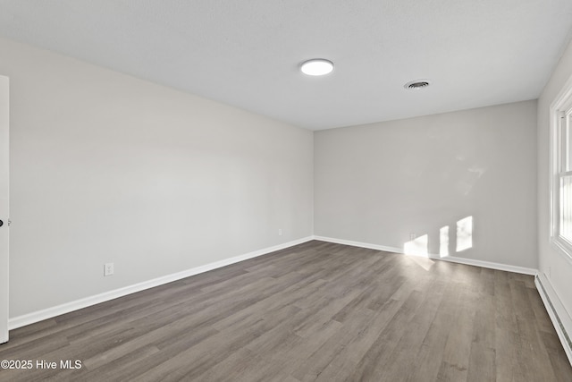 empty room with dark wood-type flooring, a wealth of natural light, and a baseboard radiator