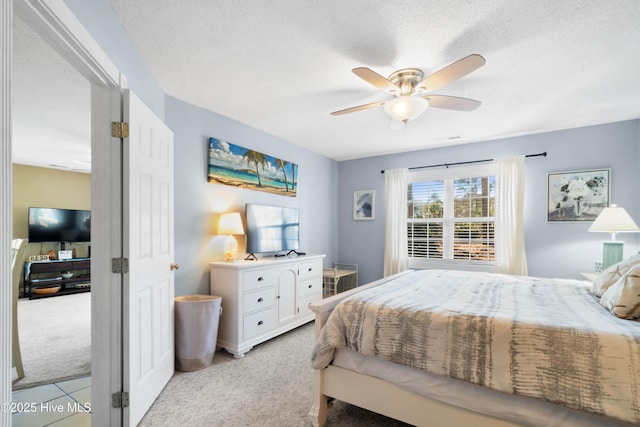 bedroom with ceiling fan, light colored carpet, and a textured ceiling