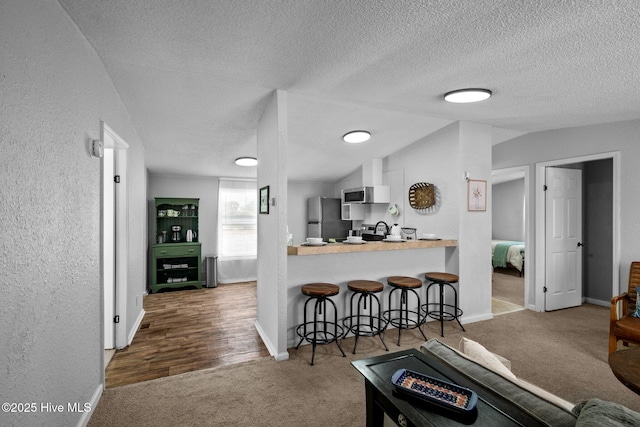 kitchen with vaulted ceiling, carpet flooring, appliances with stainless steel finishes, kitchen peninsula, and a breakfast bar area