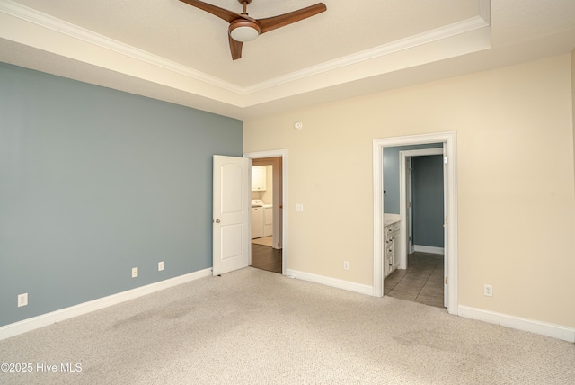 unfurnished bedroom with ensuite bath, washer and dryer, ceiling fan, a tray ceiling, and light colored carpet