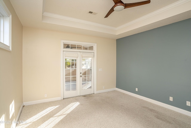 carpeted empty room with ceiling fan, a raised ceiling, ornamental molding, and french doors