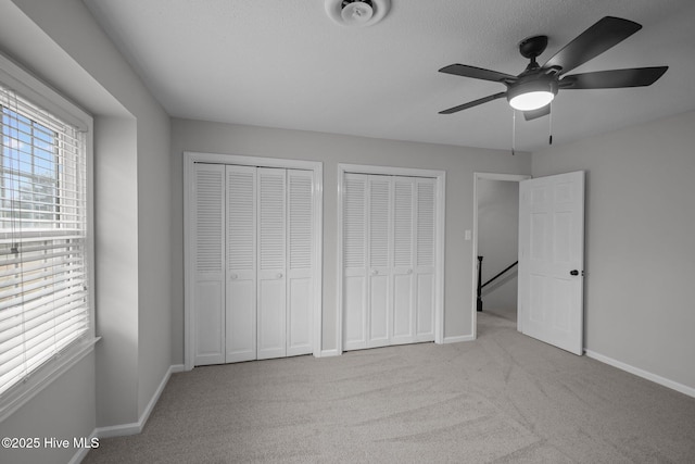 unfurnished bedroom with light carpet, multiple windows, ceiling fan, and multiple closets