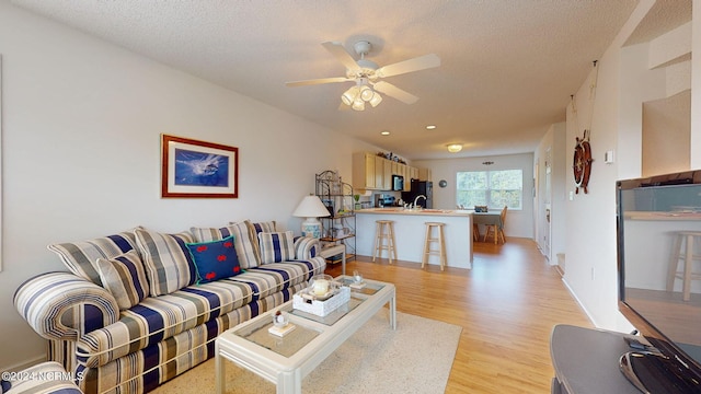 living room featuring a textured ceiling, light hardwood / wood-style floors, ceiling fan, and sink